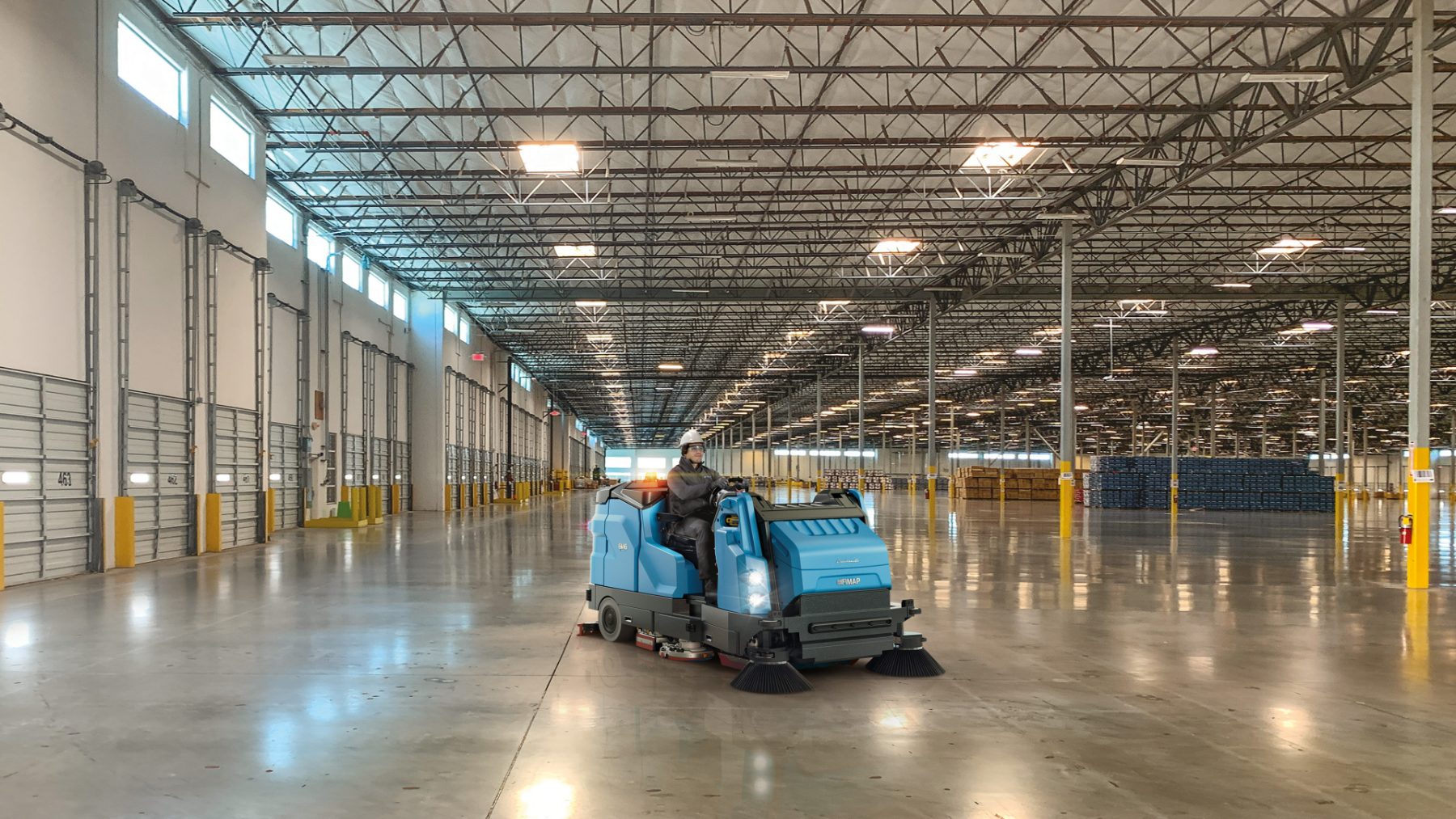 Ride-on combination sweeper scrubber working a logistics warehouse aisle