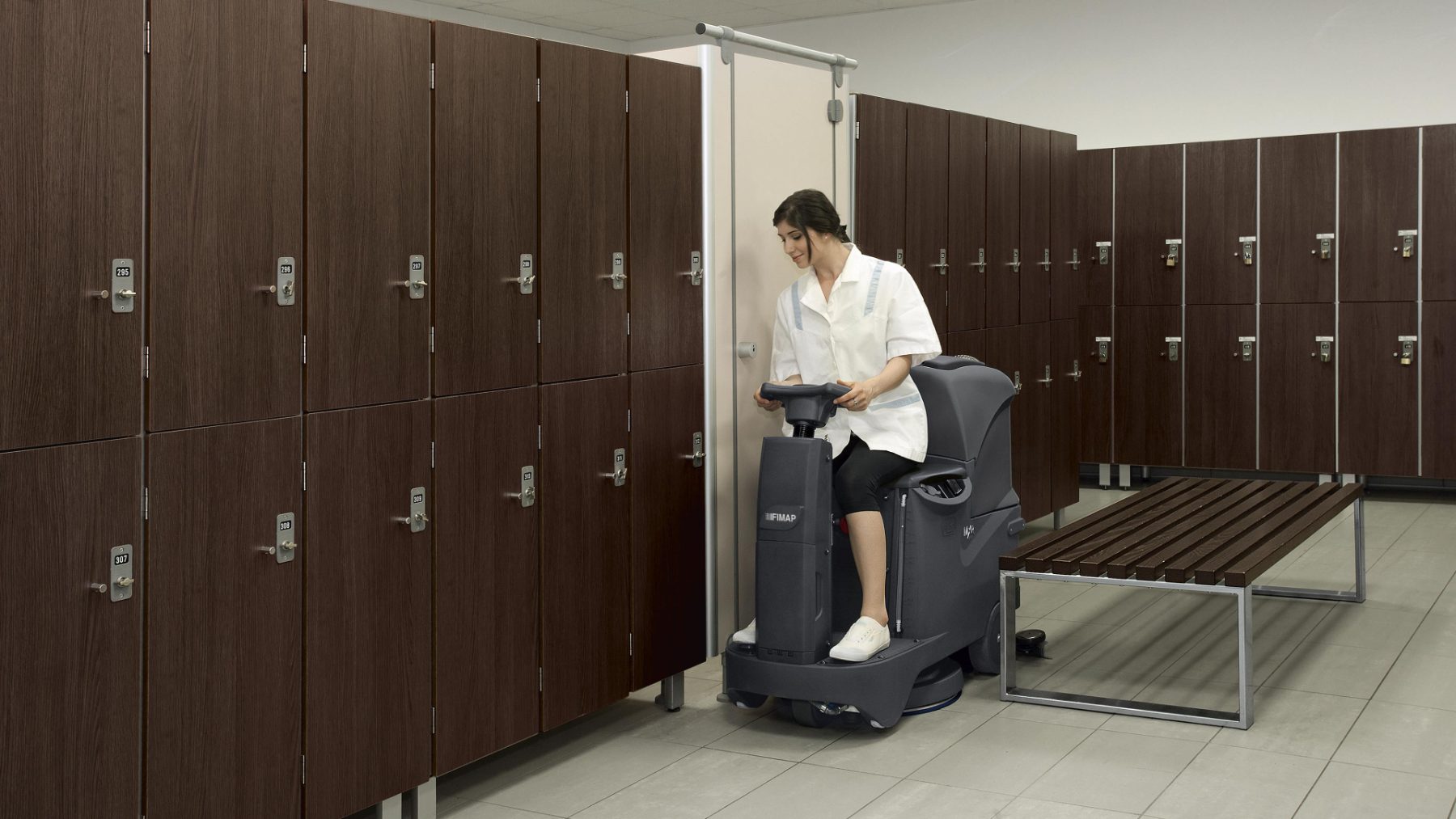 Compact ride-on scrubber cleaning a change room between rows of lockers