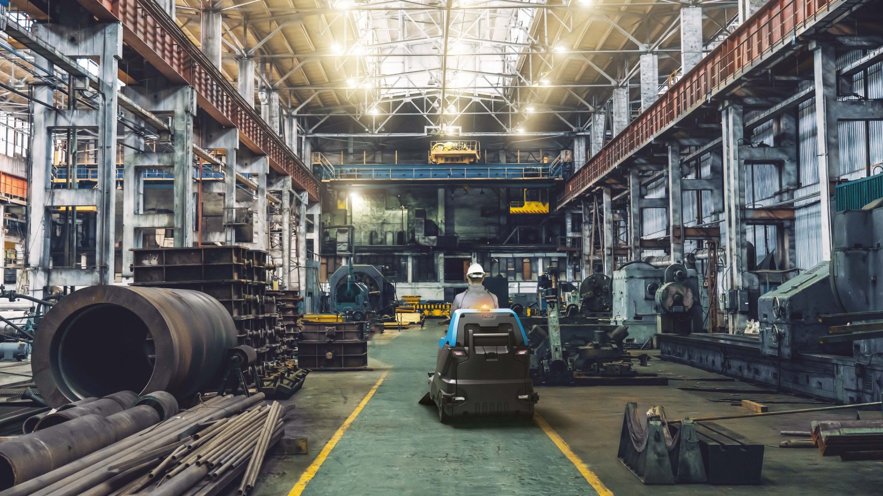 Ride-on sweeper working the main aisle of a heavy engineering workshop