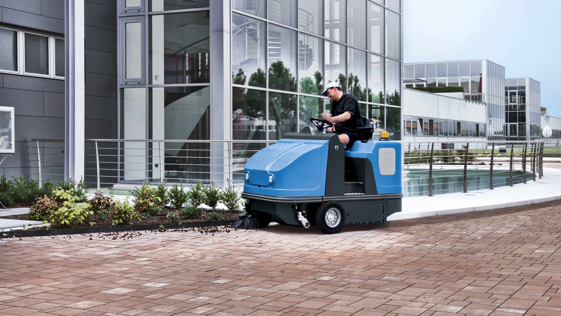 Ride-on sweeper cleaning a paved outdoor forecourt