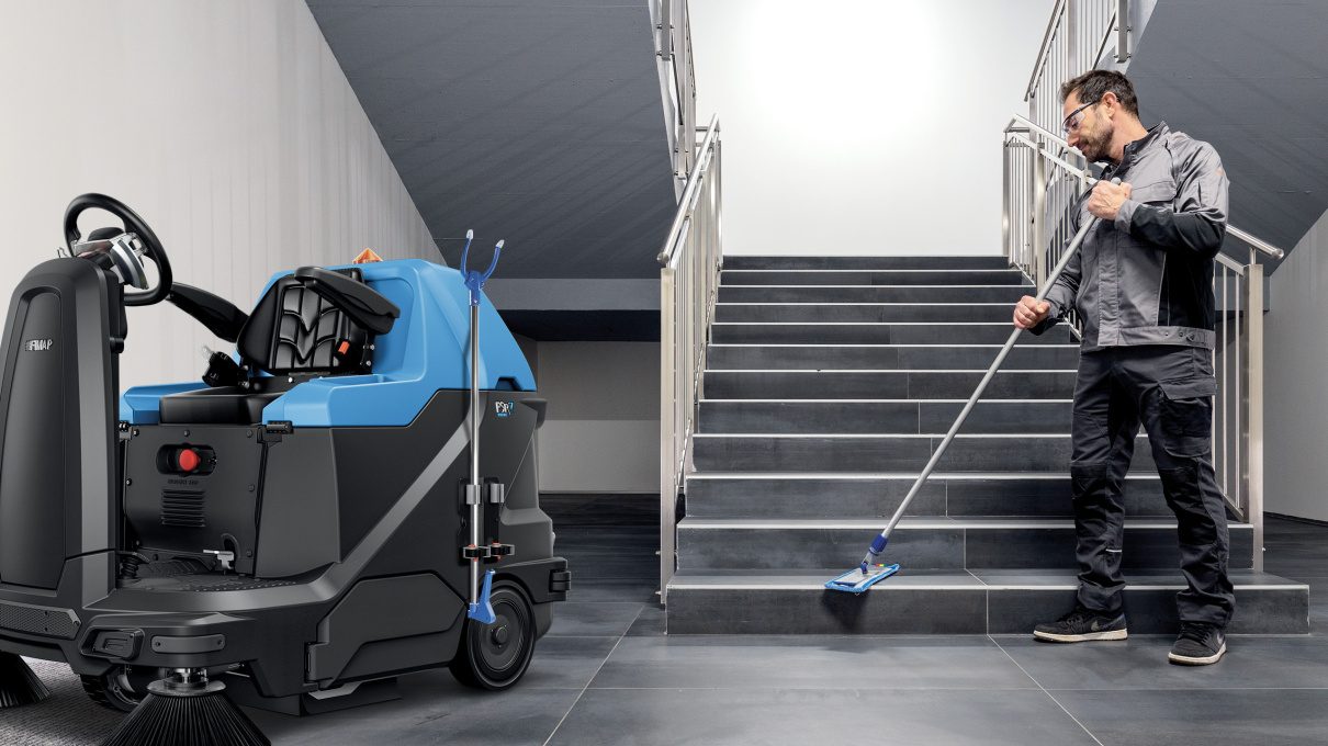 Floor machine parked beside an operator mopping stairs in a commercial building