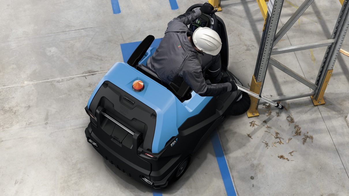 Operator adjusting the side brush on a ride-on industrial sweeper